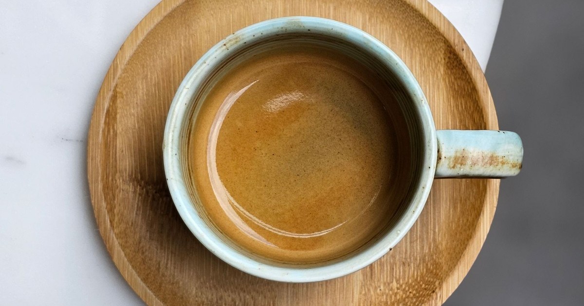A single freshly brewed espresso in a plain ceramic cup on a light marble table, viewed from above