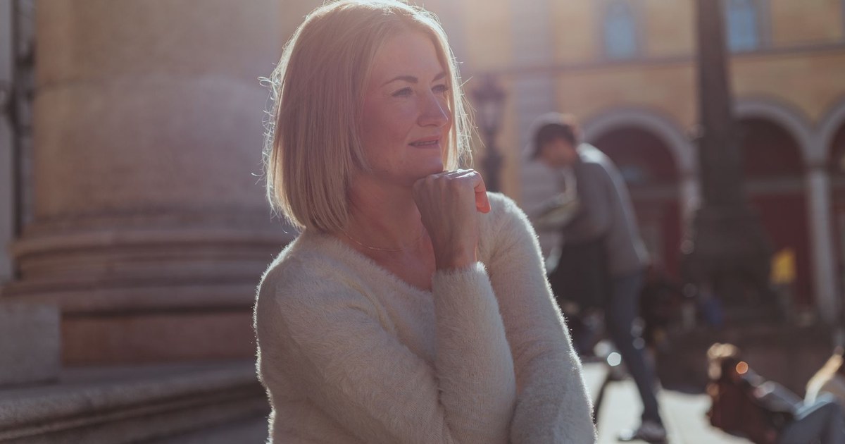 A calm, healthy middle-aged woman relaxing outdoors in soft natural sunlight, looking content and well