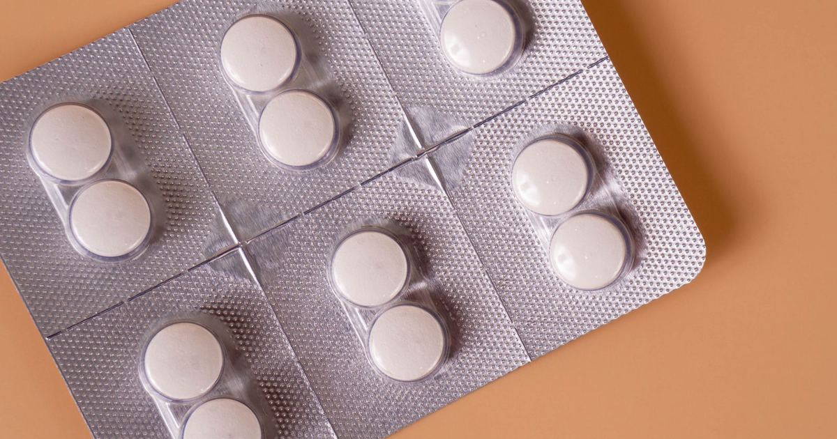 A silver blister pack of round white tablets on a peach background