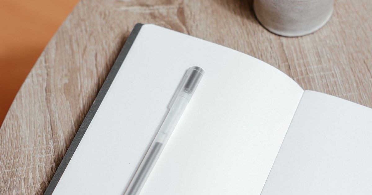 An open notebook and pen beside a cup of coffee on a desk