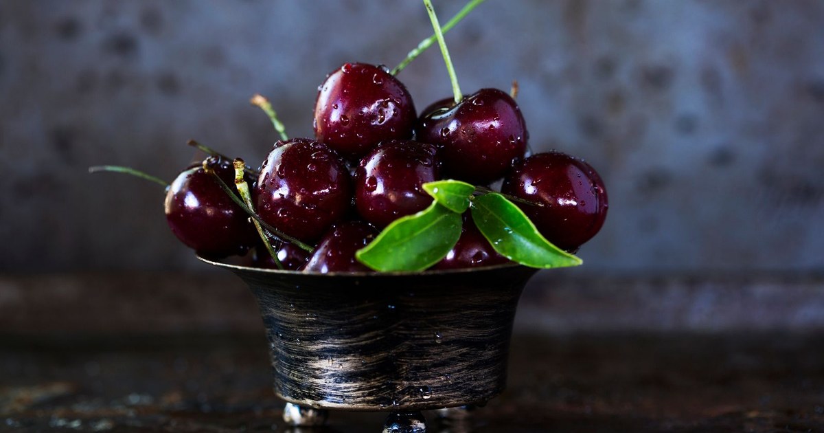 A rustic dark metal bowl filled with fresh glossy red cherries on a wooden surface