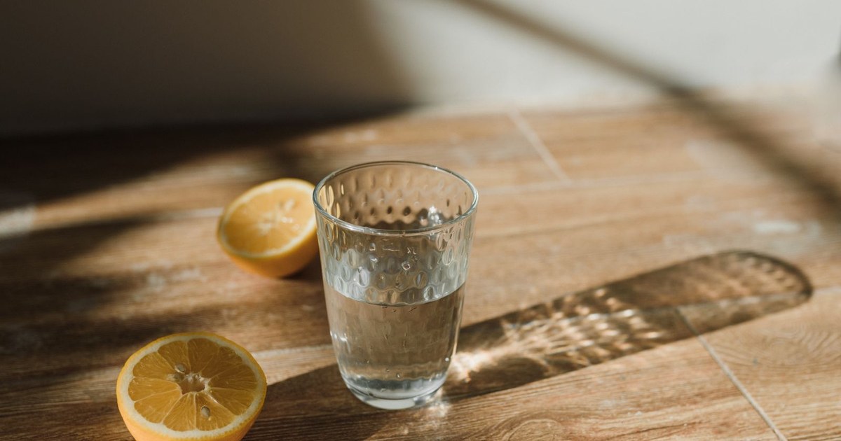A tall glass of water beside fresh lemon halves on a sunlit wooden kitchen counter