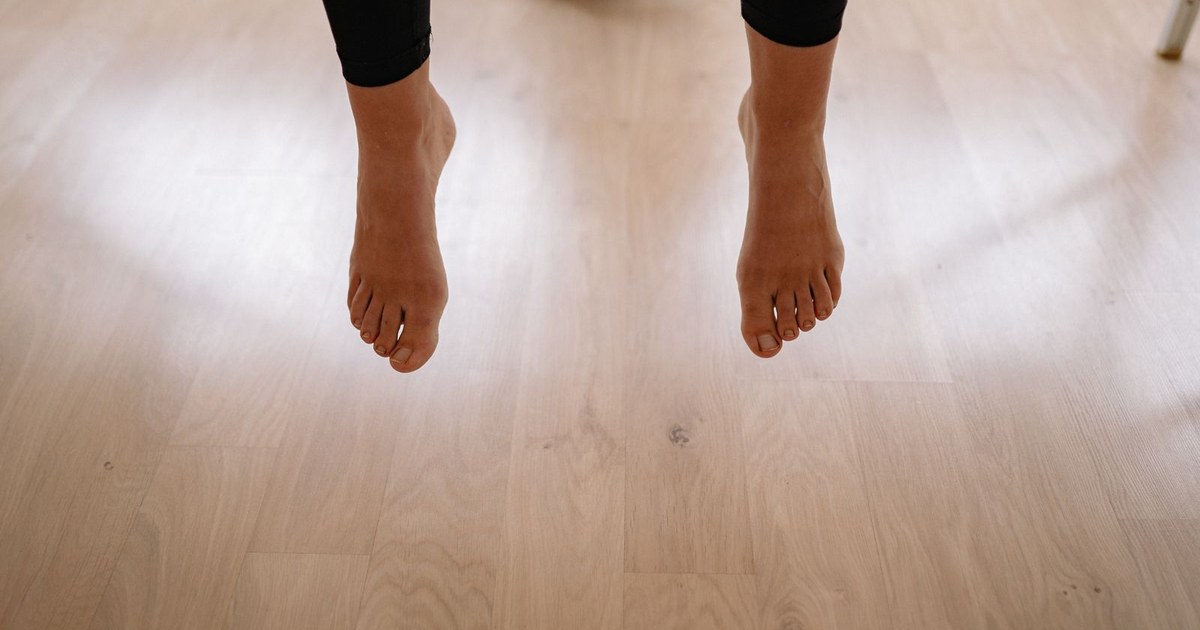 A person's two bare feet resting just above a light wood floor in a bright calm room