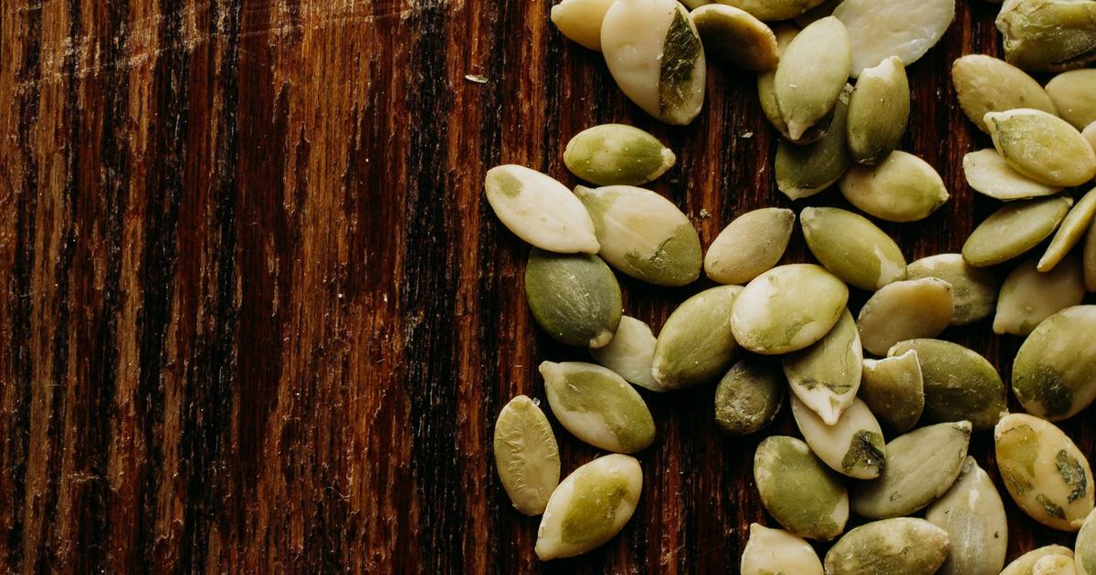 A scattered pile of raw green pumpkin seeds on a rustic wooden table in soft natural light