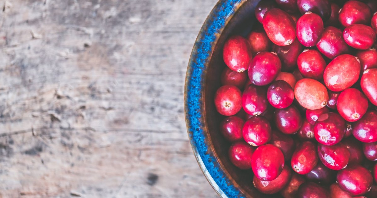 Fresh red cranberries filling a blue rimmed ceramic bowl set on a weathered rustic wooden table