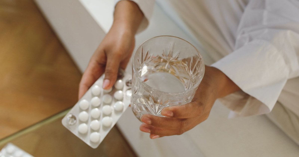 A person's hands holding several supplement capsules next to a glass of water
