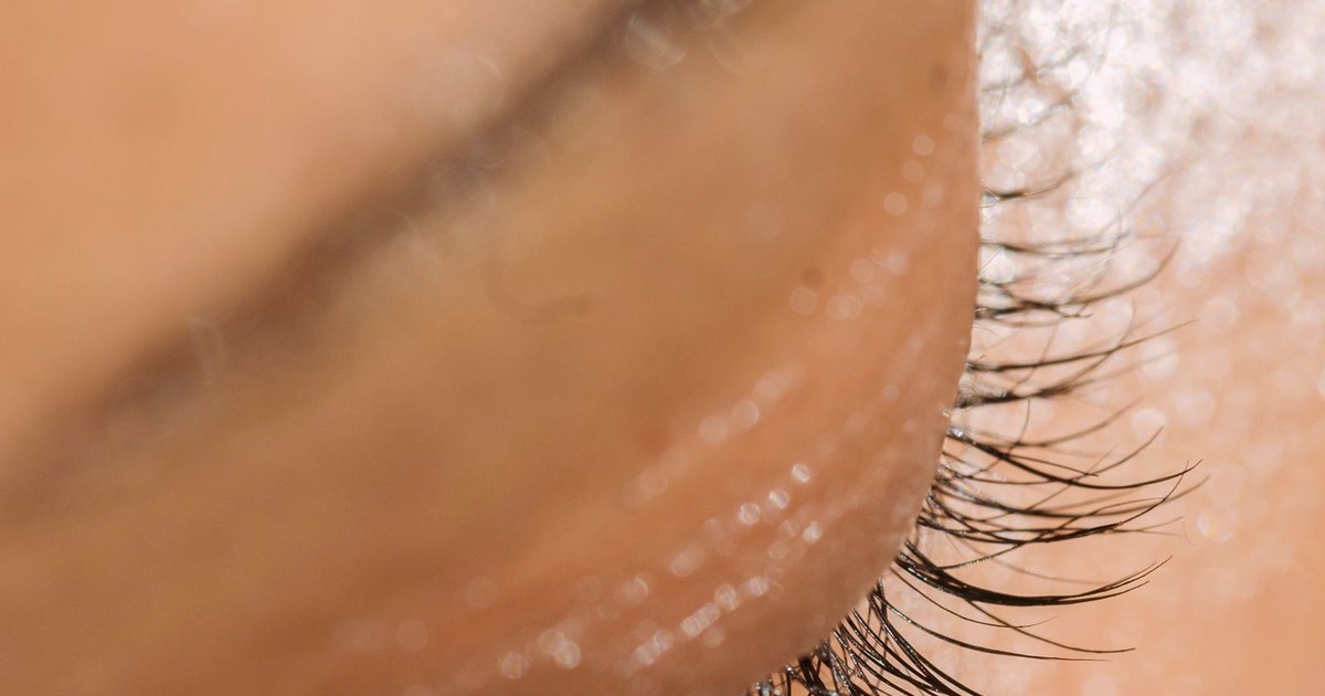 Extreme close-up of the eye area of an adult with dewy, smooth, glowing skin and natural eyelashes