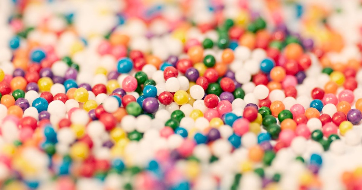 Close-up of tiny rainbow-colored round candy sprinkles packed in a dense multicolored pile