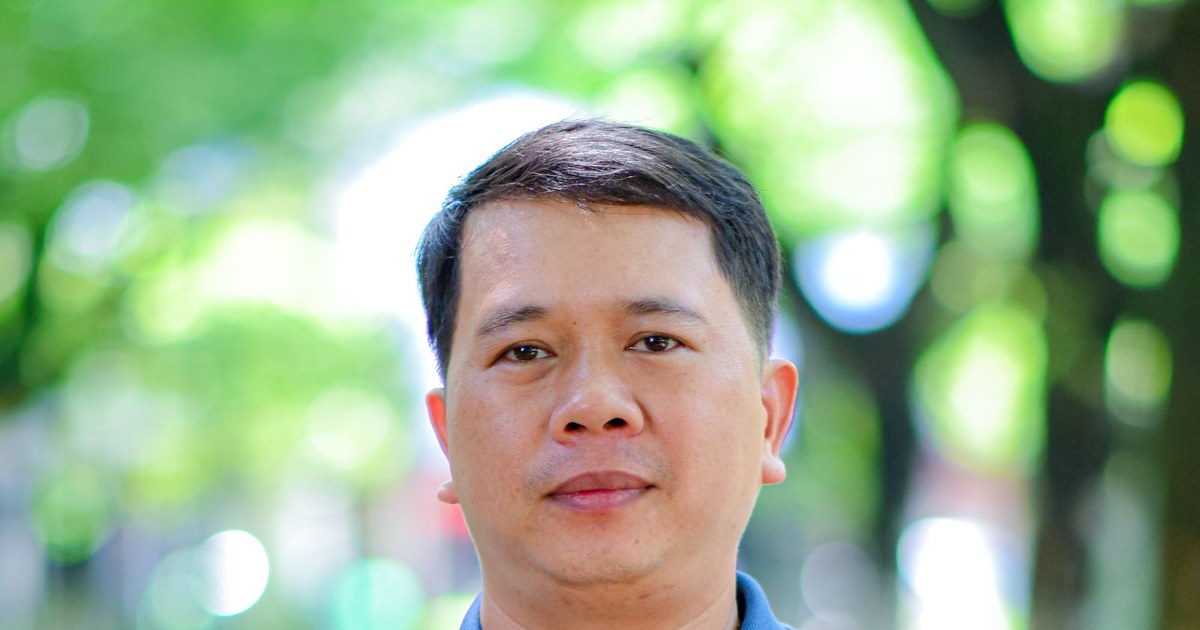 A calm, confident middle-aged man outdoors with soft green foliage behind him