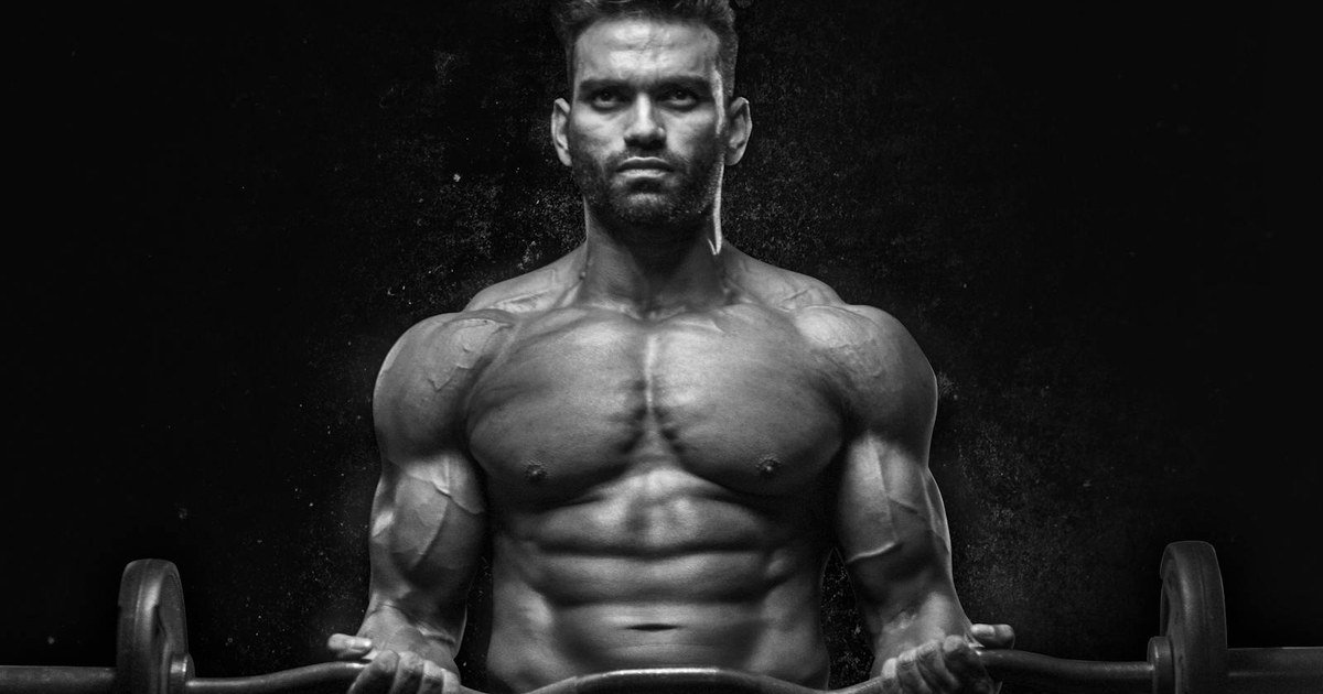 A muscular man holding a barbell in a moody black and white gym portrait
